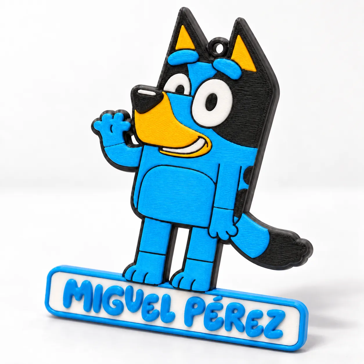 Etiqueta para mochila con la figura de Bluey y el nombre Miguel Pérez, impresa en 3D en azul, negro y amarillo