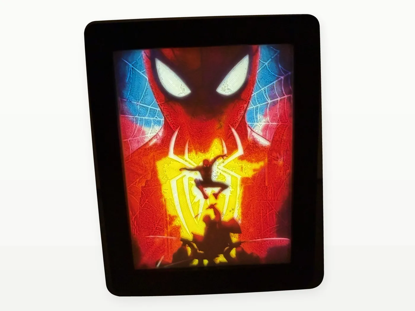 Litofanía de Spider-Man encendida, con la máscara en rojo y azul y la araña amarilla, en marco negro