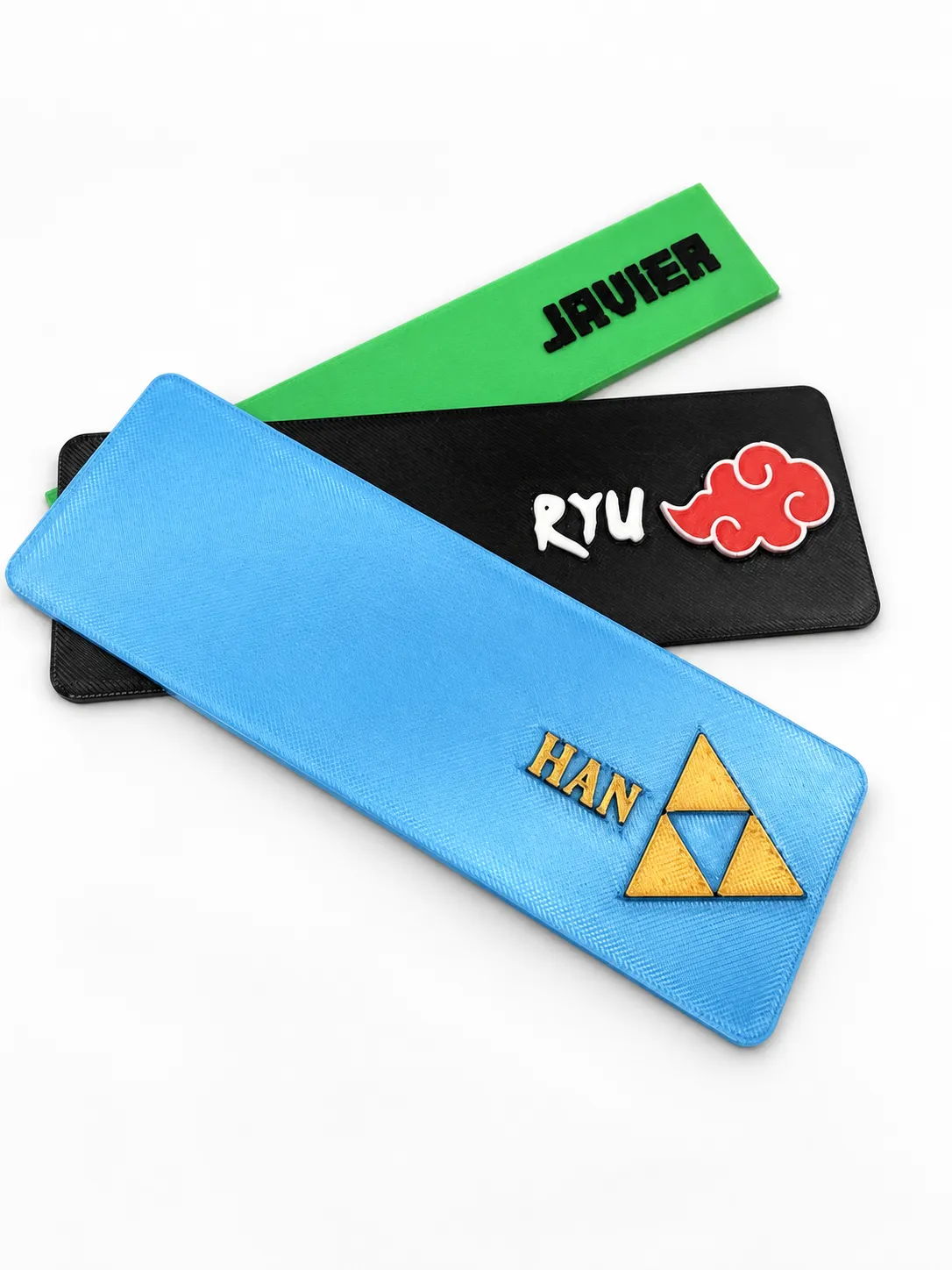 Marcapáginas personalizados con los nombres Javier, Ryu y Han, con la nube Akatsuki de Naruto y la trifuerza de Zelda, impresos en 3D